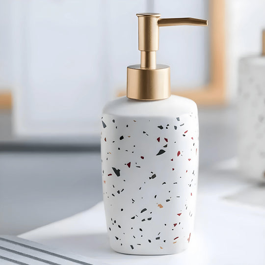 Trio of white matte ceramic soap dispensers with gold pumps in various geometric shapes on a bathroom tray.