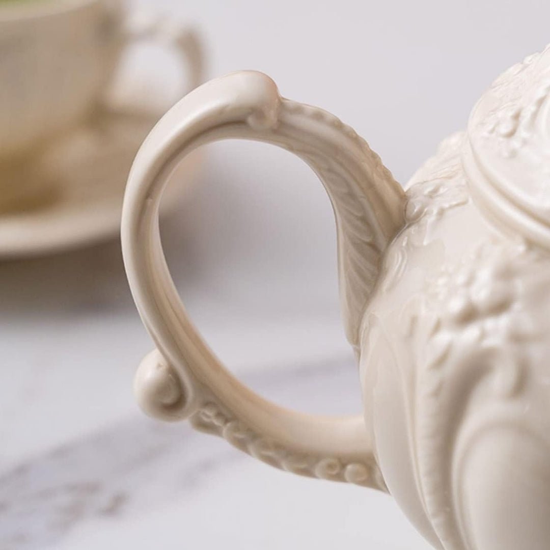 Vintage beige porcelain teapot with floral palace-style embossed design and matching teacup on marble surface