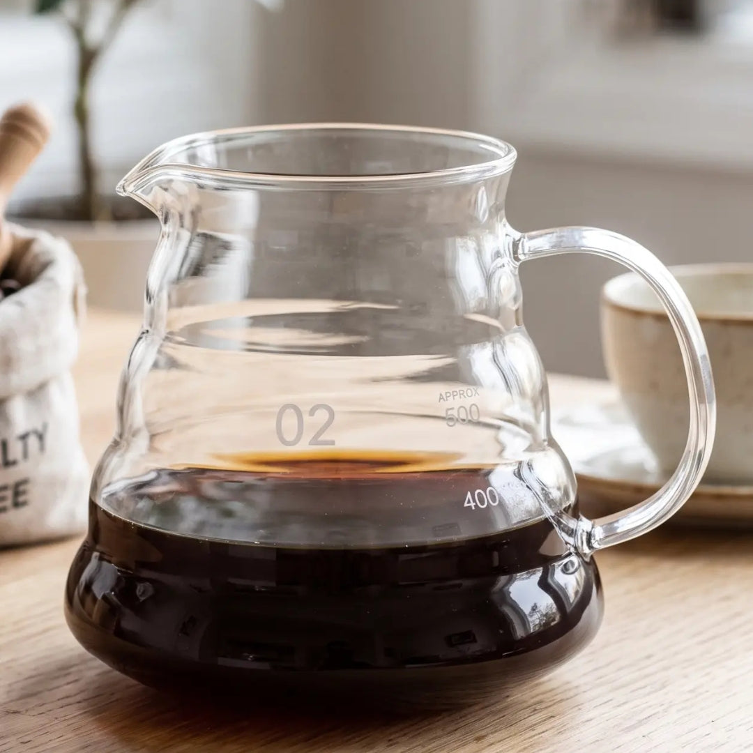 600ml clear glass coffee server without a lid, partially filled with coffee on a clean ivory background.
