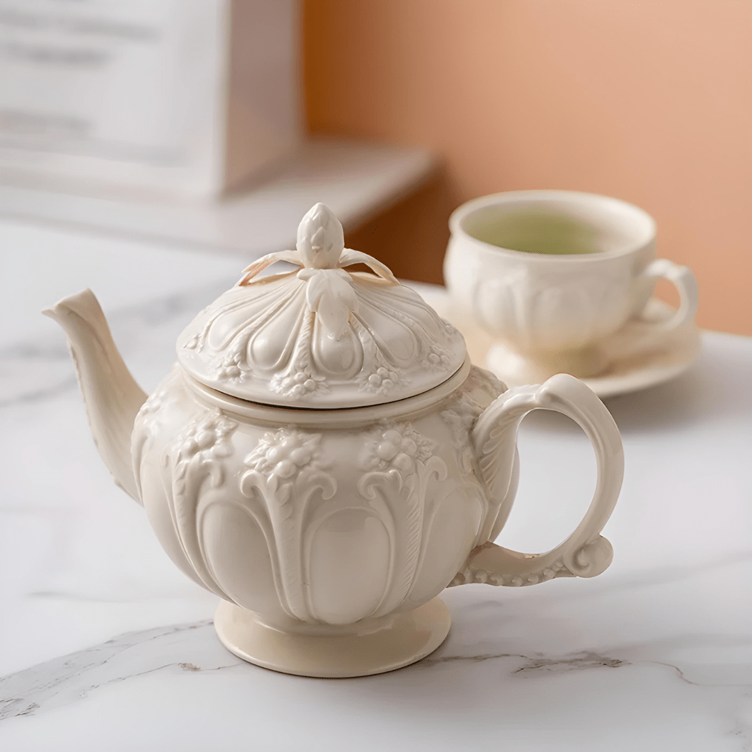 Vintage beige porcelain teapot with floral palace-style embossed design and matching teacup on marble surface

