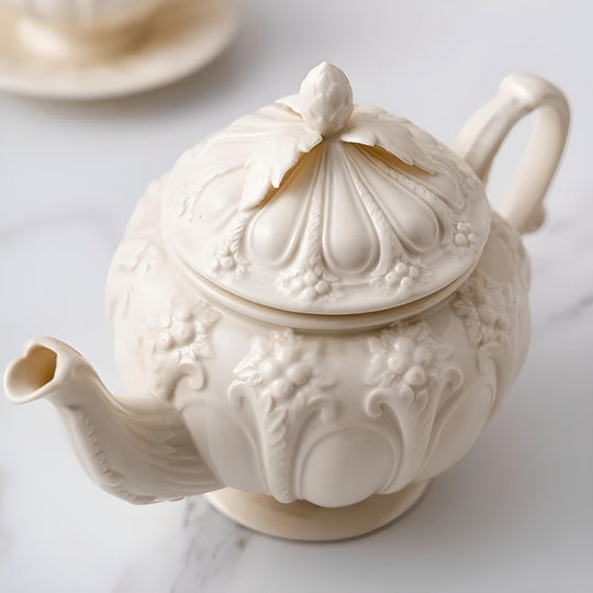 Vintage beige porcelain teapot with floral palace-style embossed design and matching teacup on marble surface

