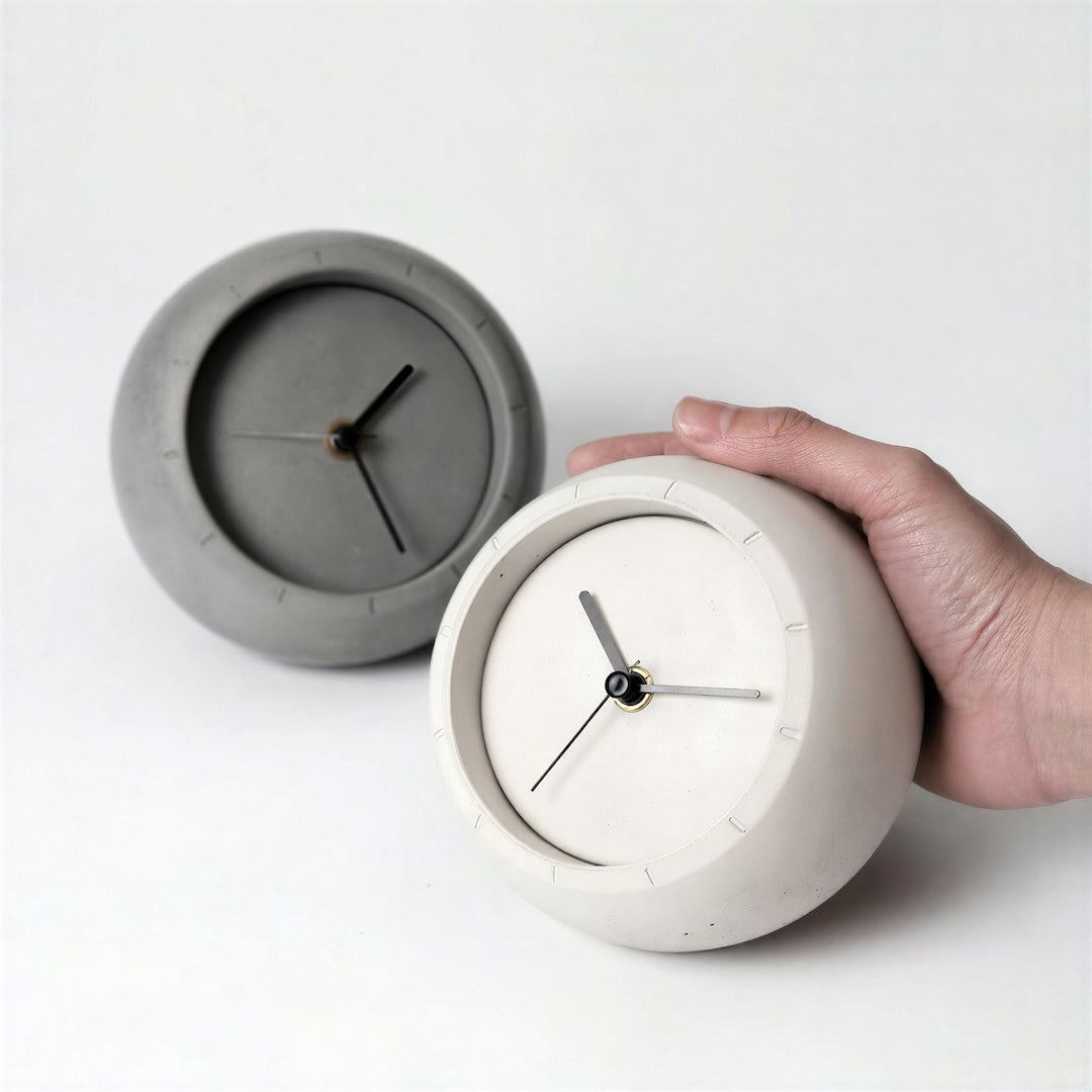 Compact ivory concrete desk clock held in hand with grey clock behind it