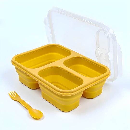 Yellow silicone food container with compartments and a lid, accompanied by a yellow fork and spoon on a white background.